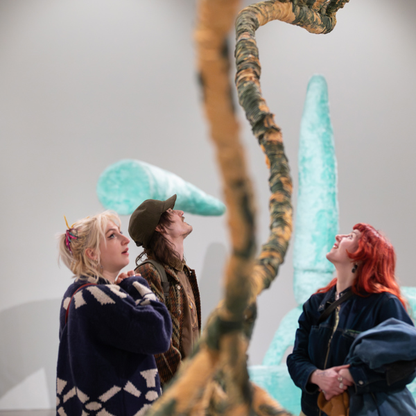 Three visitors look up at large abstract sculpture in an art gallery