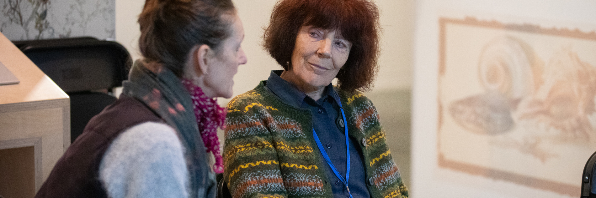 A photograph of two people sat down in conversation in the Ruskin Gallery at Millennium Gallery.