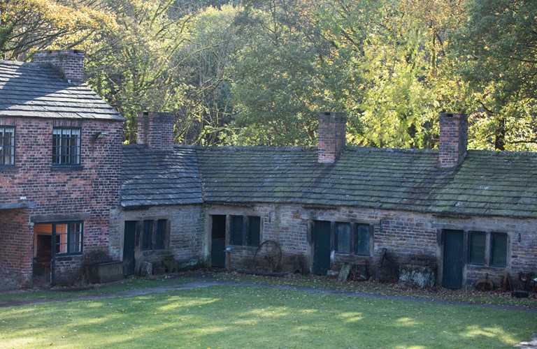Old stone roofed workshops in a sunny woodland setting.