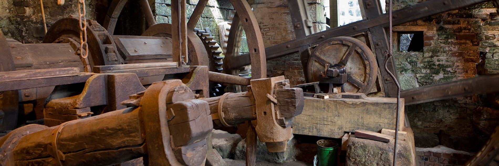 Two rusting tilt forge hammers mounted on huge old timber shafts with gearwheel drive mechanisms in the background.
