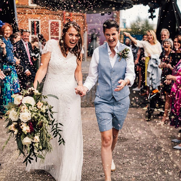 Two adults in wedding outfits being showered with confetti by a crowd of people under the Bessemer Converter
