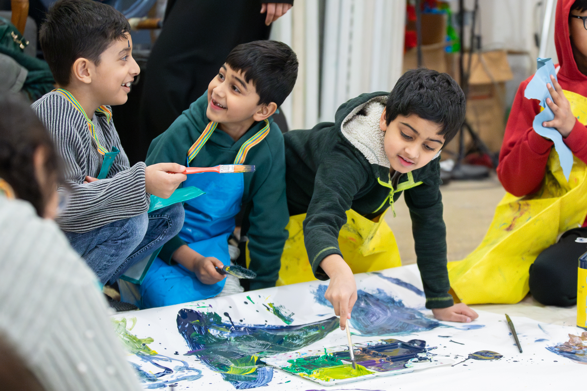 Children smile and chat as they kneel on teh floor and contribute to a large-scale artwork