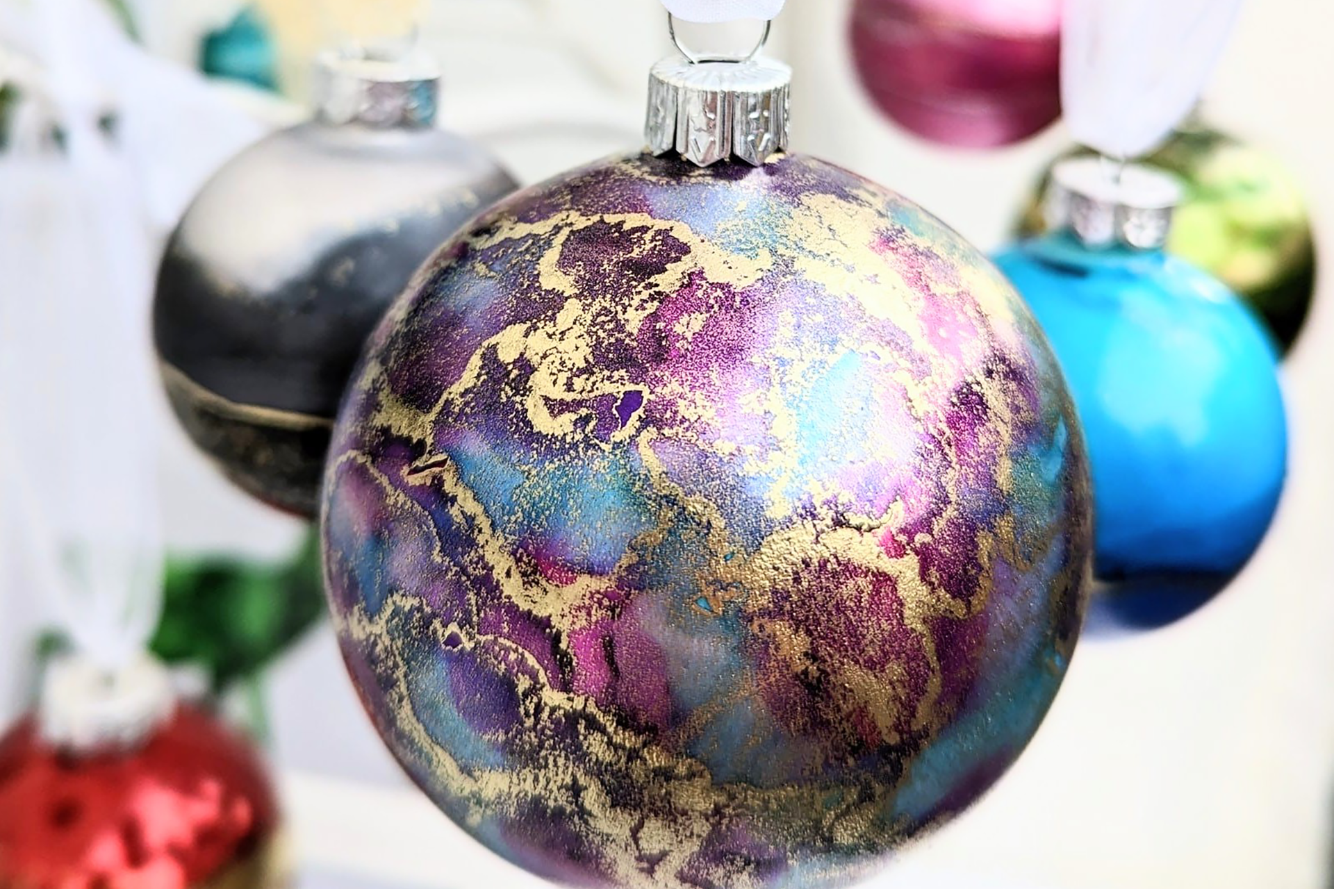 A close up of a purple bauble with swirls of gold and blue ink patterns. Other baubles can be seen in the background.