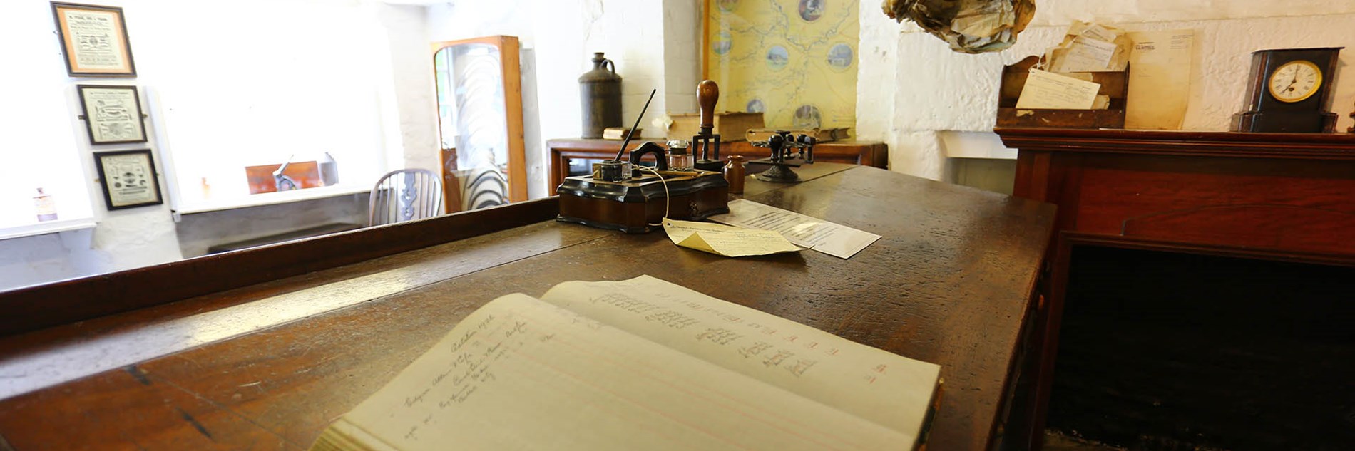 Internal view of Counting House looking across old desk with open ledger and various items of period office equipment.