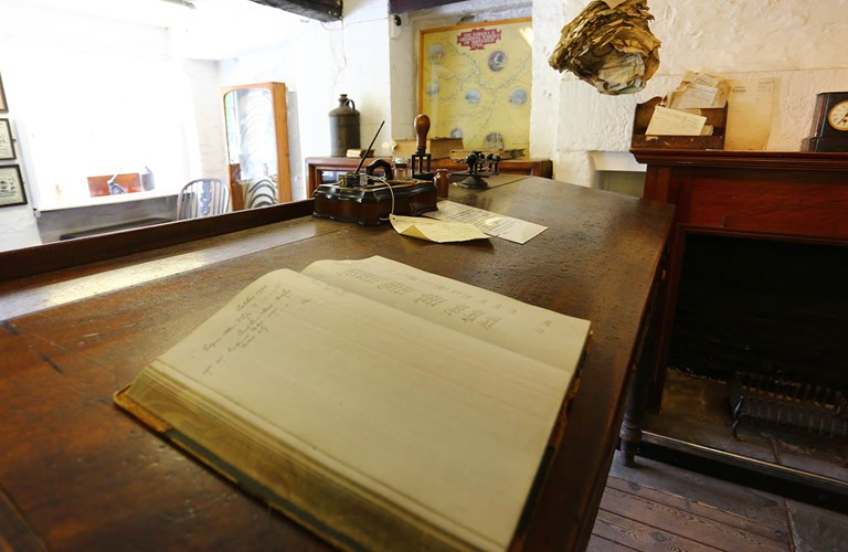 Internal view of Counting House looking across old desk with open ledger and various items of period office equipment.