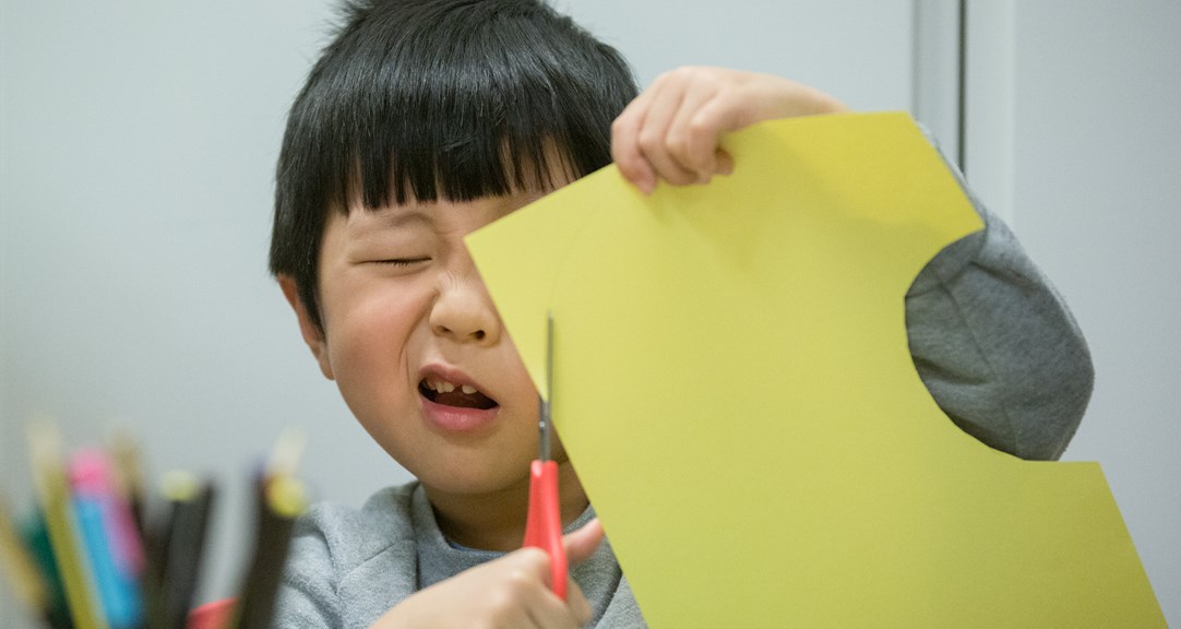A very focused child cutting paper held close to their face. 