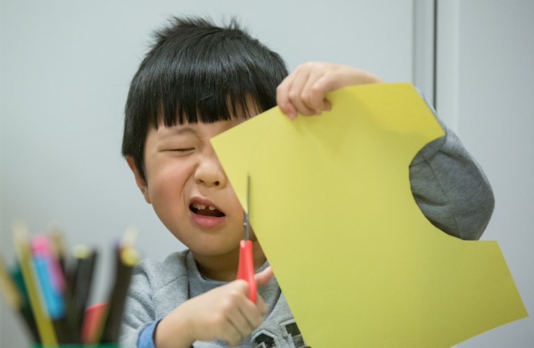 A very focused child cutting paper held close to their face. 