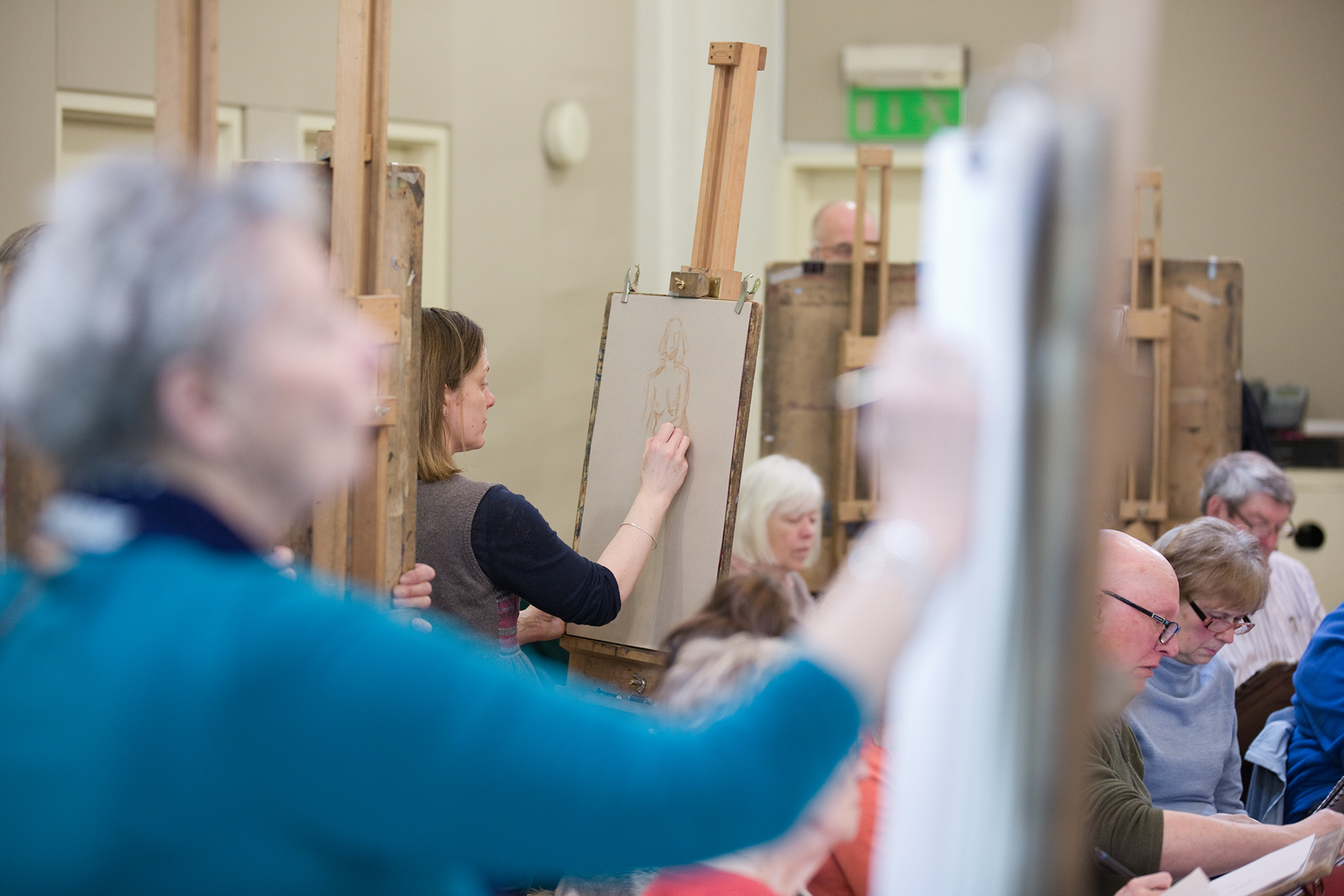 A group of artists standing at easels and sitting at desks drawing. 