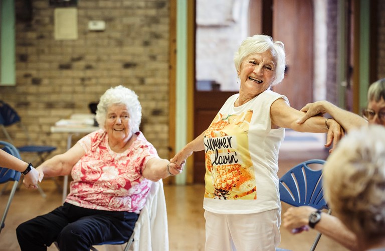 A group of seated and standing older adults linking arms whilst dancing