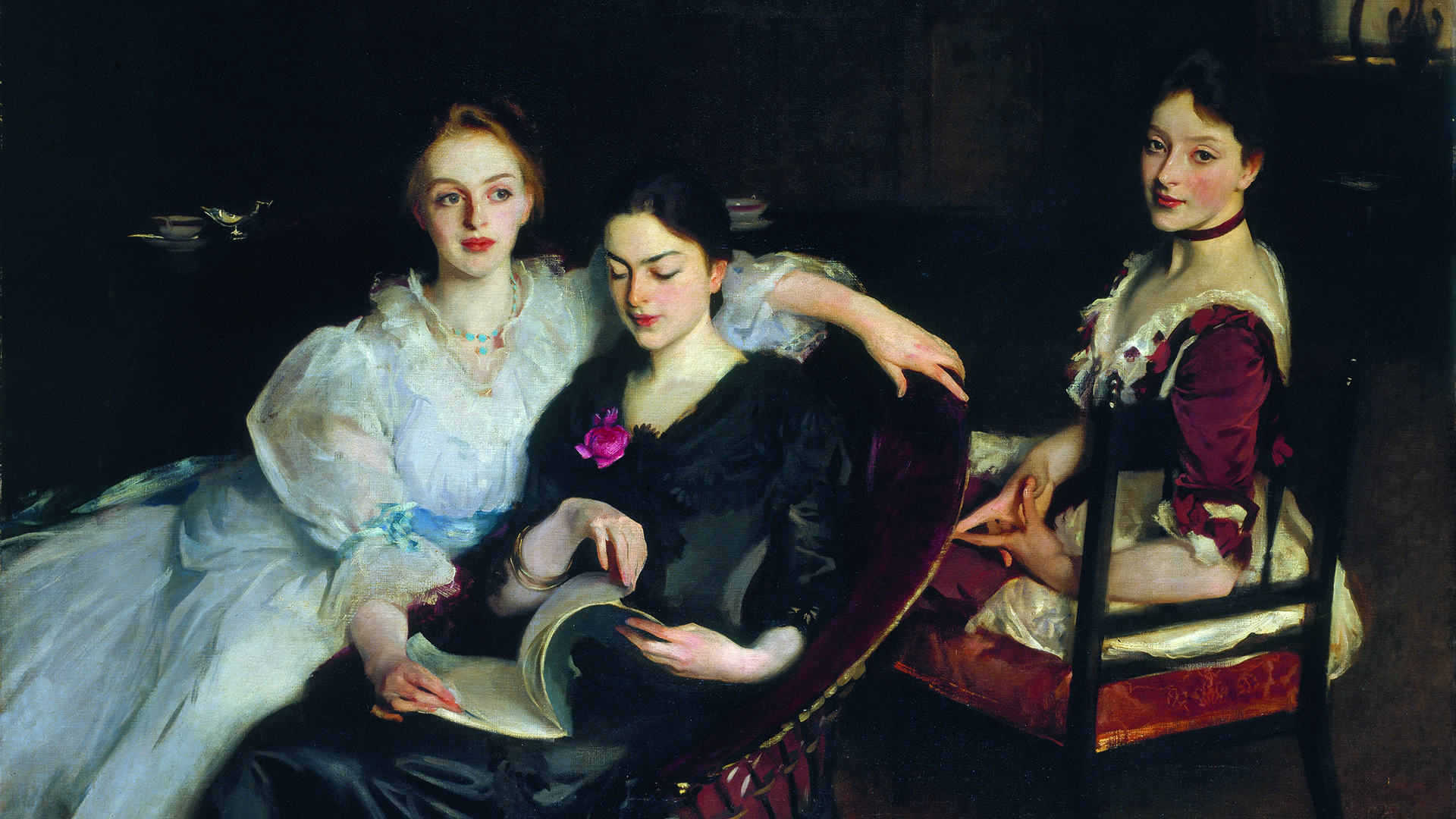 An oil painting of three women in formal Victorian dress. They are sitting informally next to each other - two women are sharing a chair and looking at a book, and the third woman is sitting on a chair behind them. The painting has a dark background, with the outline of a dresser on which sits a silver jug and a porcelain bowl. 