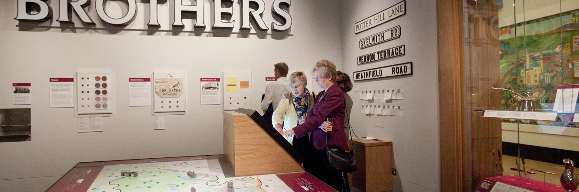 A large sign above a map, with four adults looking at images on a wall and an interactive screen 