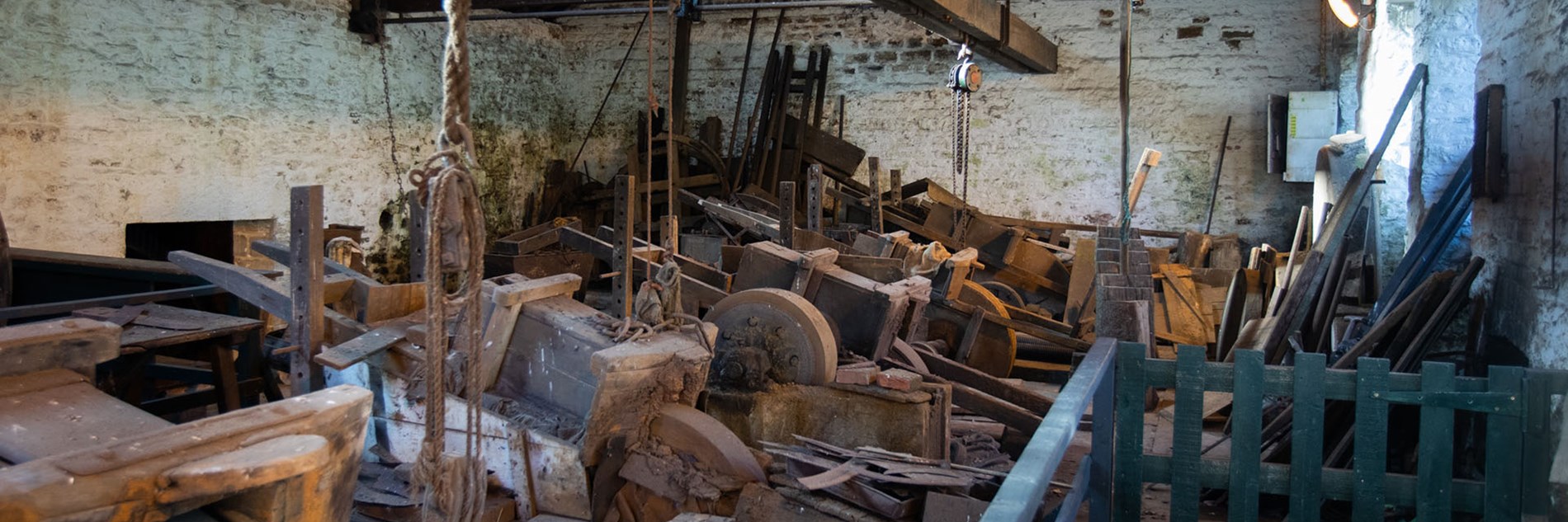 Old whitewashed workshop with exposed wooden roof beams and a row of grinding wheels with ‘saddles’.