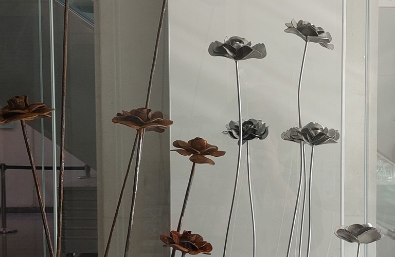 A photograph of nine steel roses inside a glass display cabinet.