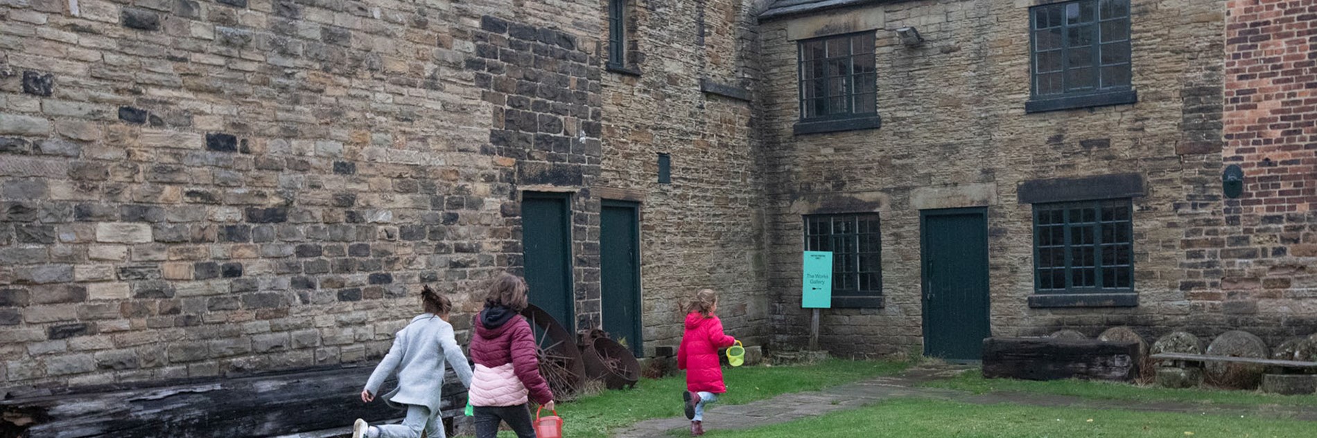 An adult and two children running across the grass towards the door of the Works Gallery.