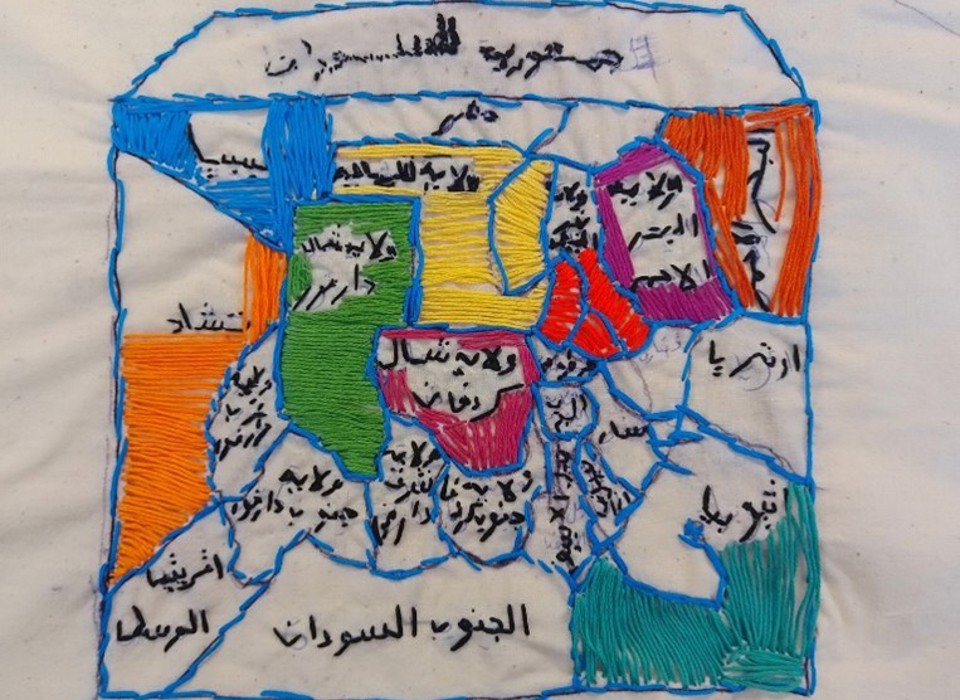 Embroidered outline of a house sectioned into brightly coloured shapes within and filled with words written in Arabic. 