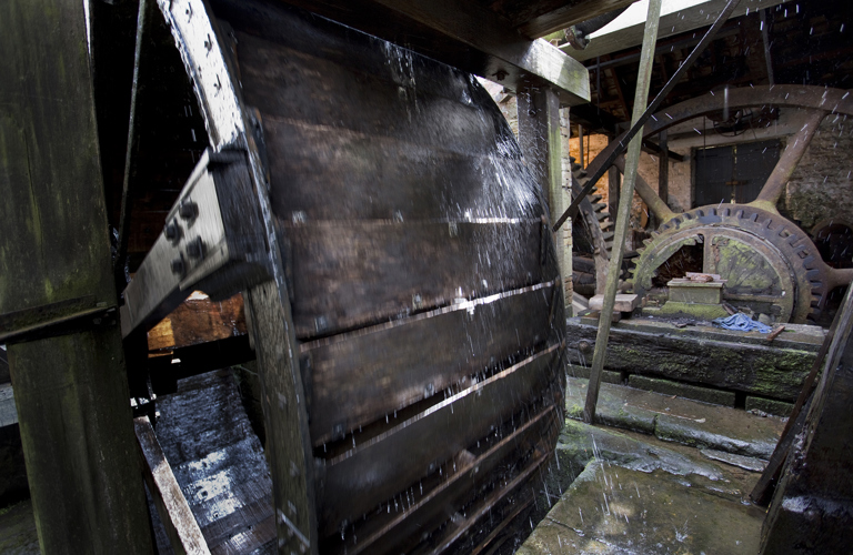 Detail of a water powered wheel with toothed flywheel in the background