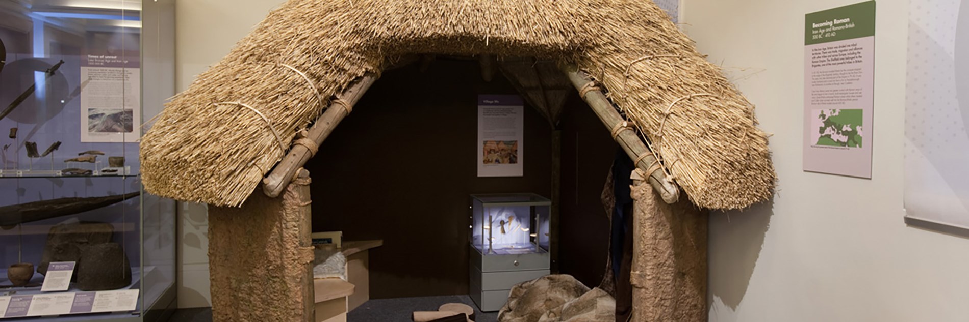 A thatched small round building with a large doorway through which you can see the interior including a replica camp fire. There are a couple of display cases inside and outside the roundhouse which hold artefacts and information sheets. 