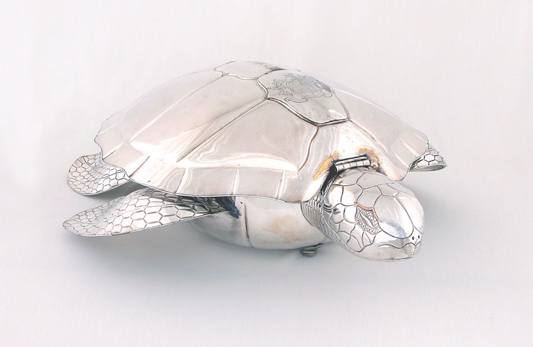 A shiny metal turtle with markings detailing its shell and flippers on a white background. 
