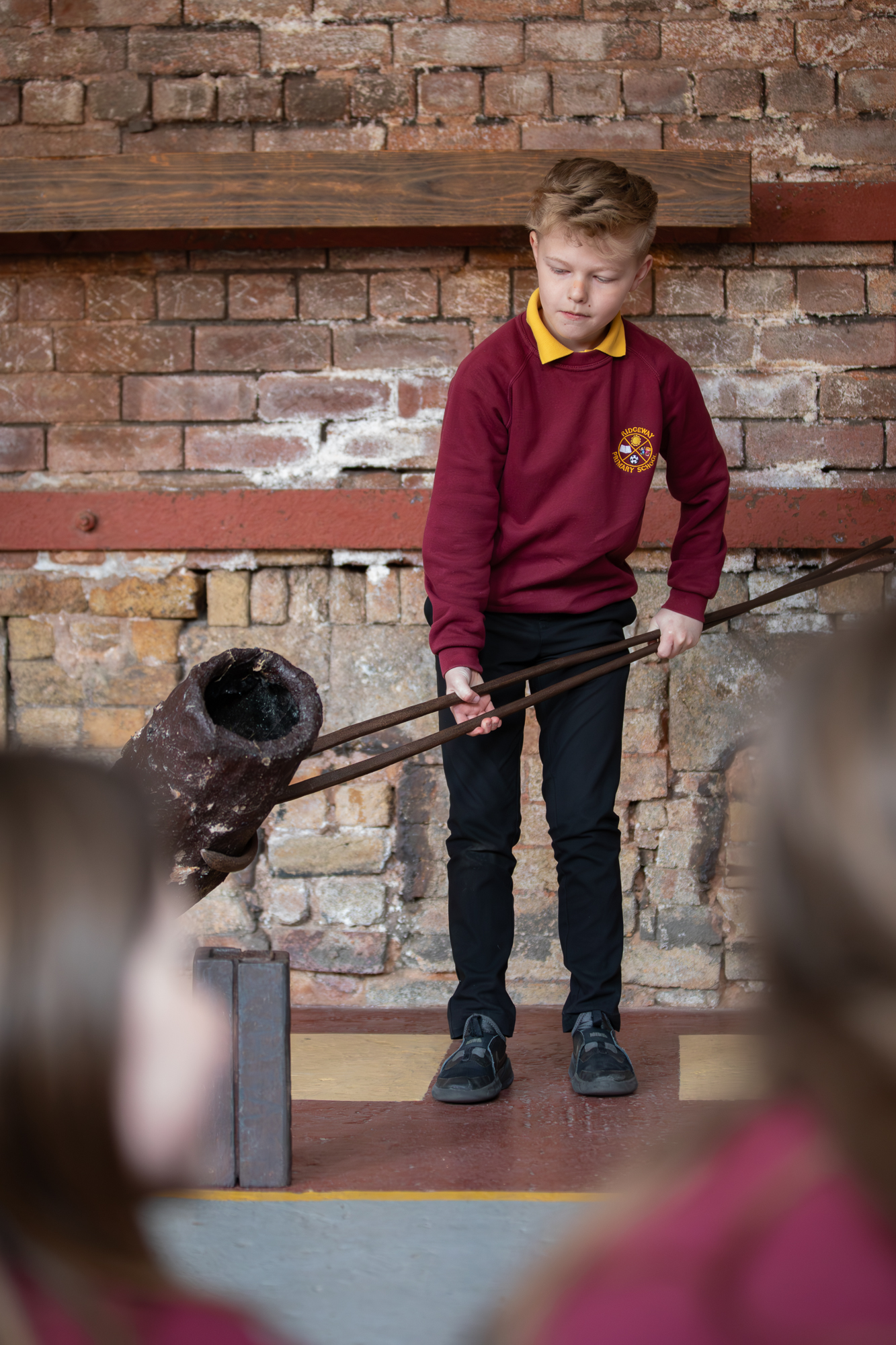 School child demonstrating how to use steel-making crucible.