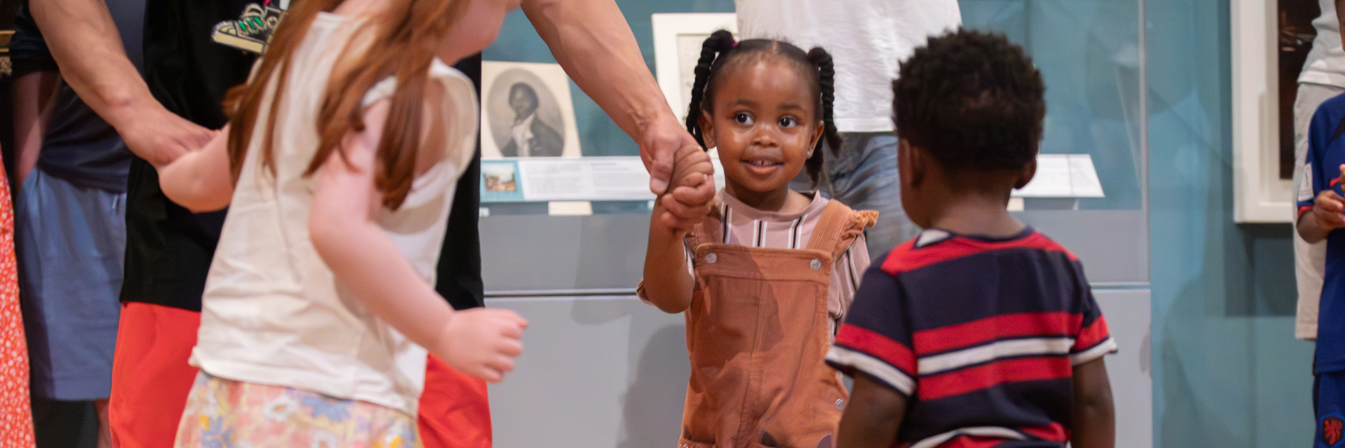 A photograph of three children holding hands with an adult in a ring, happy in a museum.