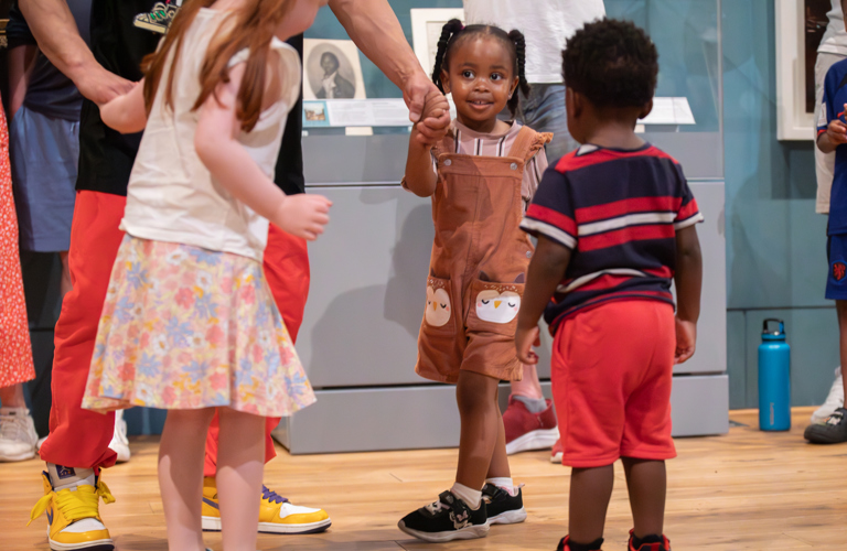 A photograph of three children holding hands with an adult in a ring, happy in a museum.