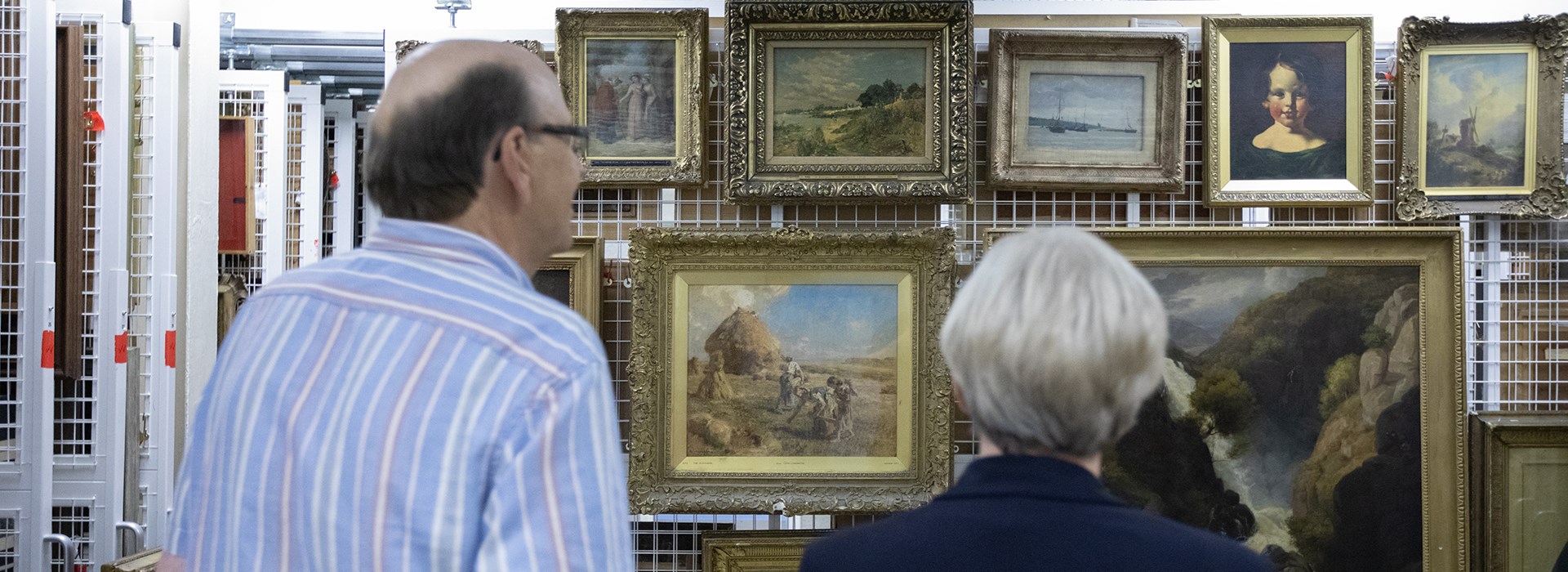 Two adults looking at a collection of framed paintings mounted on a sliding frame