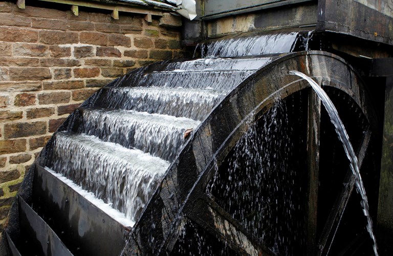 Close up of overshot waterwheel turning as it fills with running water.