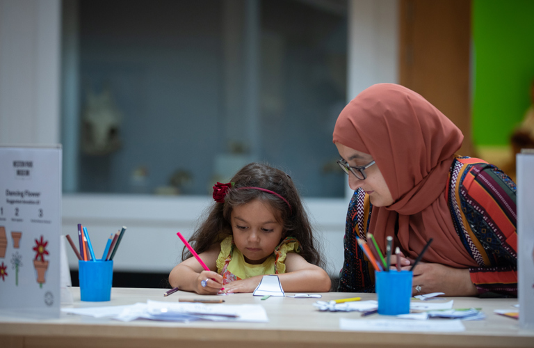 A child is carefully drawing under their parent's watchful gaze.