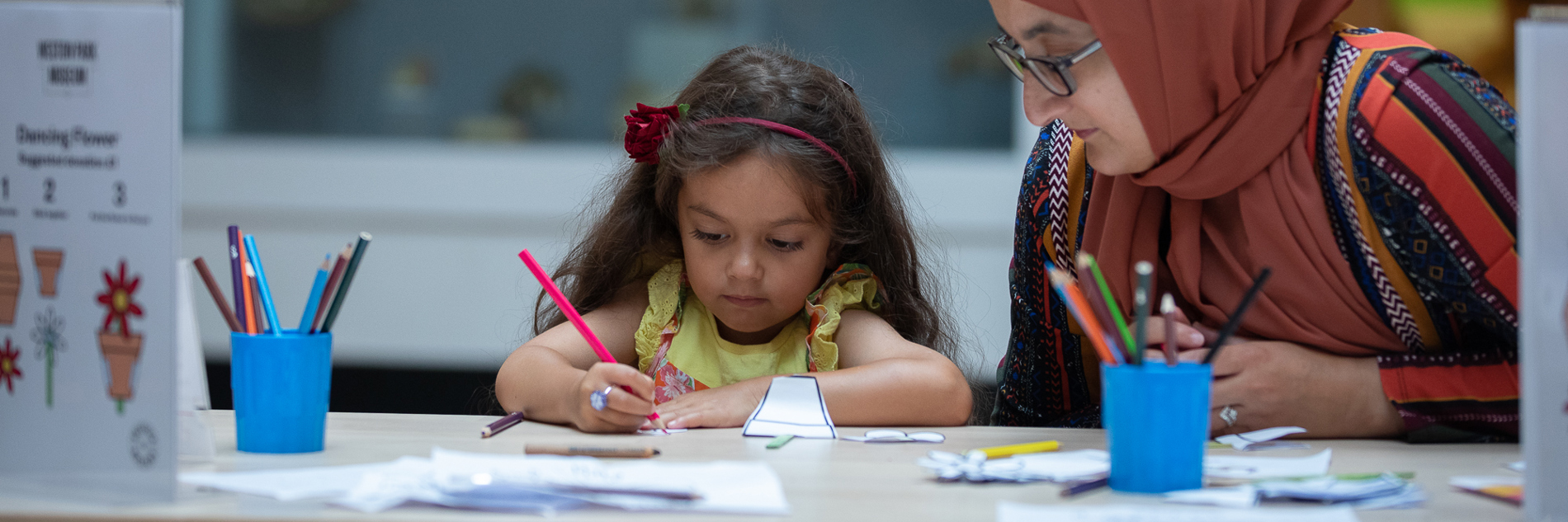 A child is carefully drawing under their parent's watchful gaze.