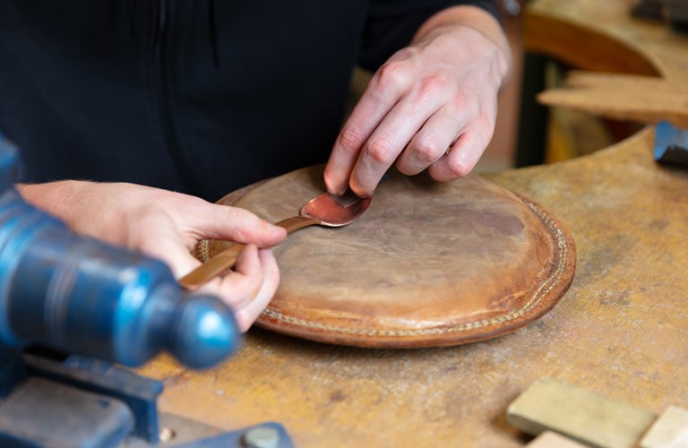 Photograph of 2 hands polishing a metal spoon on a circular leather board