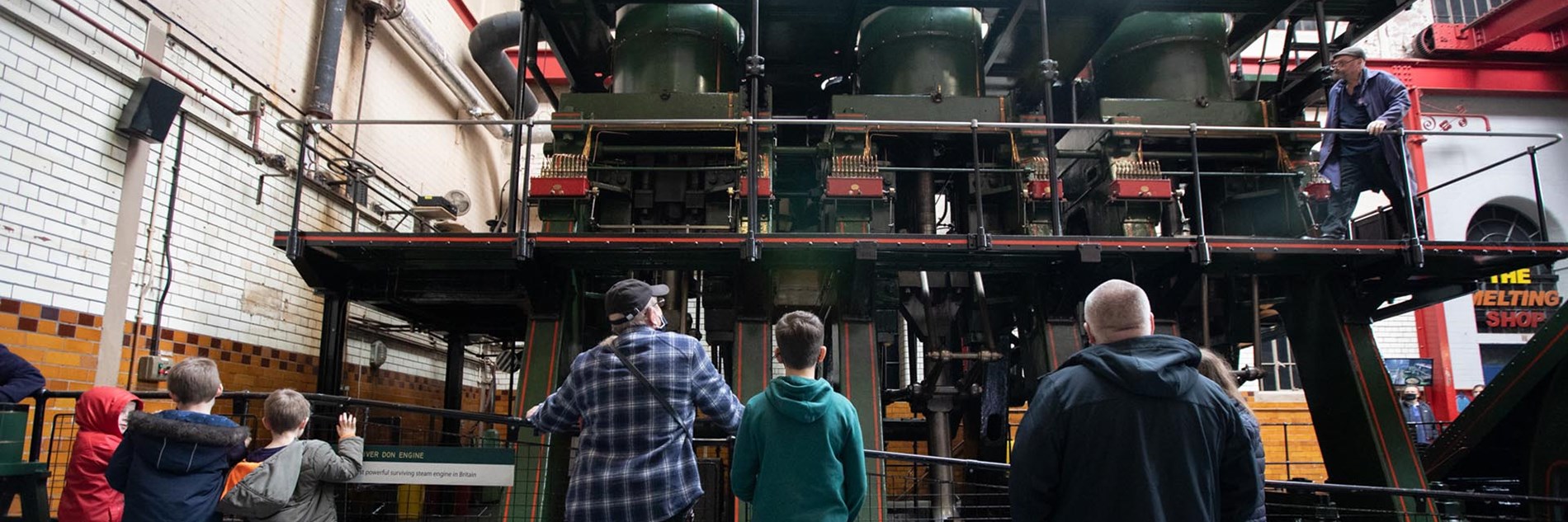 A small group of adults and children viewed from behind, looking up at the River Don Steam Engine.