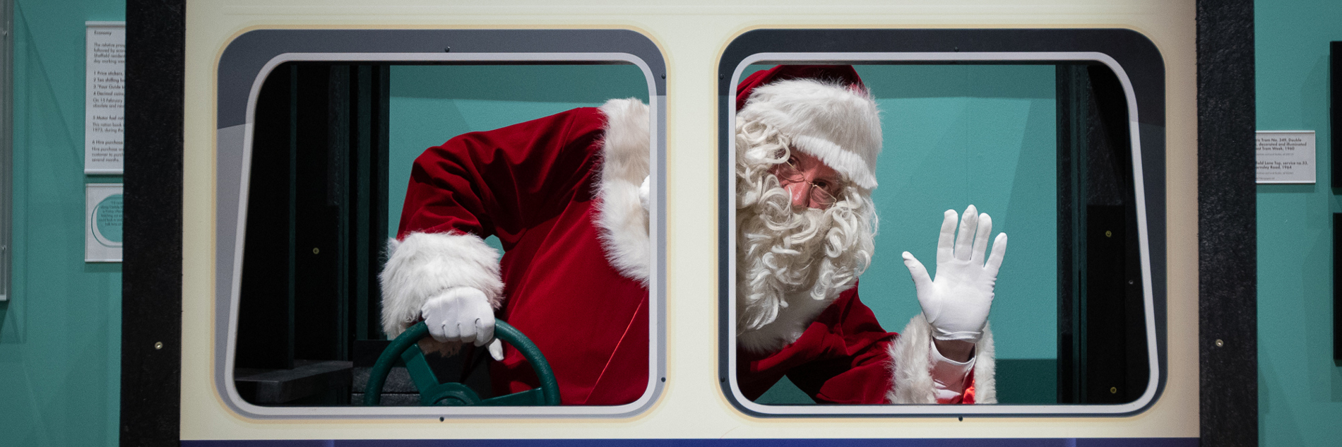 A photograph of Santa pretending to drive the tram in Weston Park Museum, waving at the camera.