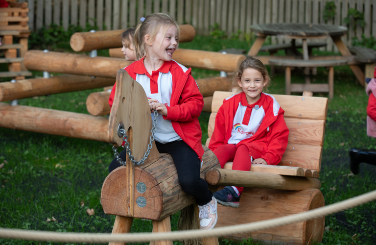 Two children play on a wooden horse and cart in a outdoor play area