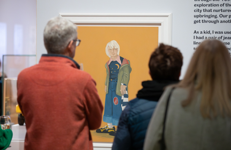 Two people look at a painting of a boy dressed in 1970s clothes 
