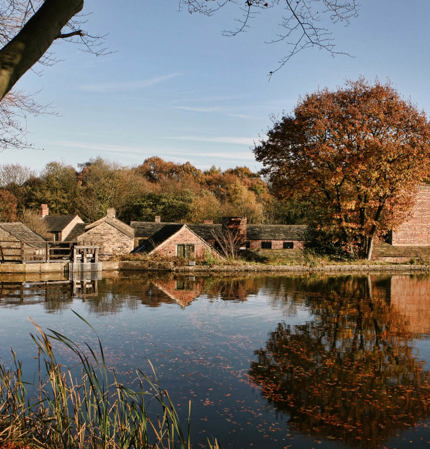 Looking across open water towards Hamlet buildings framed by trees in autumnal shades.