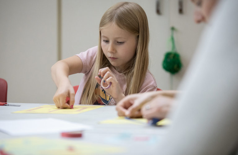 Primary-aged girl, concentrating on sticking something onto a sheet of paper.