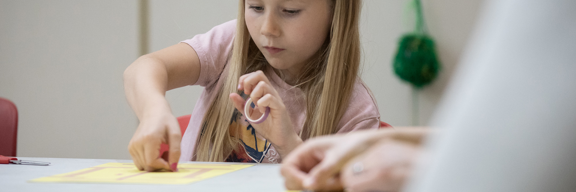 Primary-aged girl, concentrating on sticking something onto a sheet of paper.