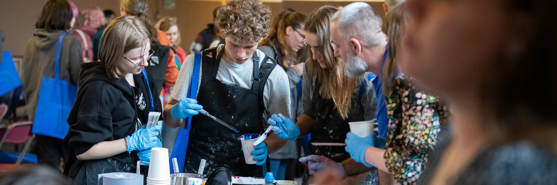 A group of young people creating something together, whilst stood around a table filled with art supplies. 