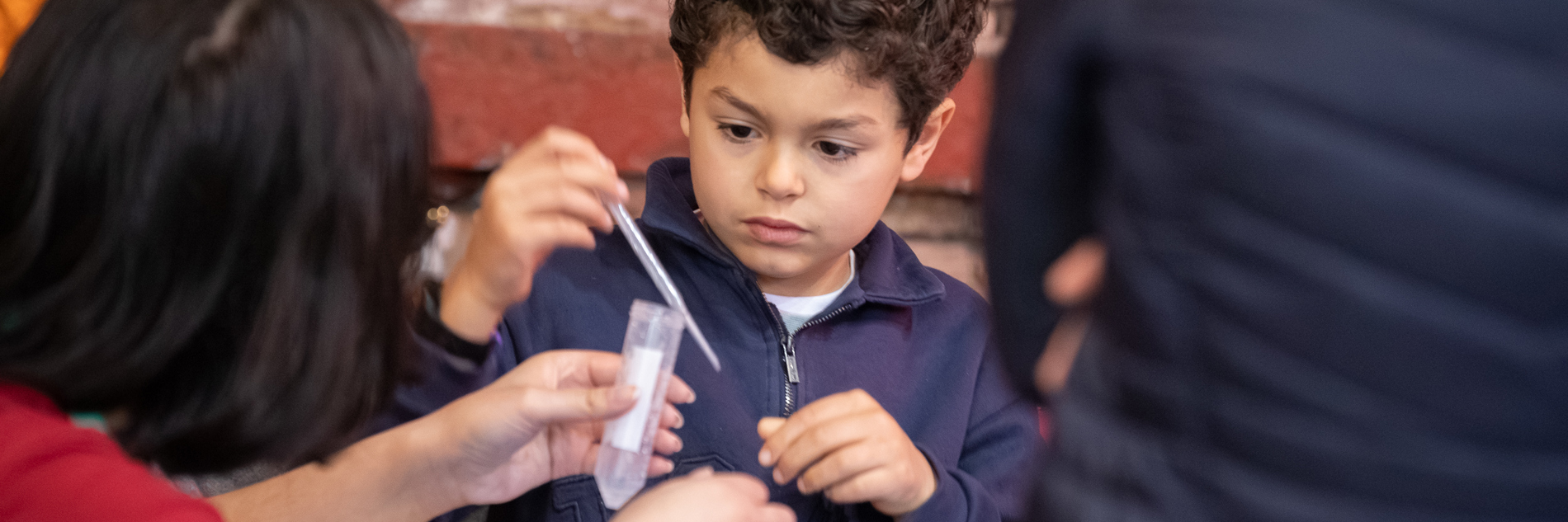 A photograph of a child holding a pipette with an adult holding a test tube in front of them. 