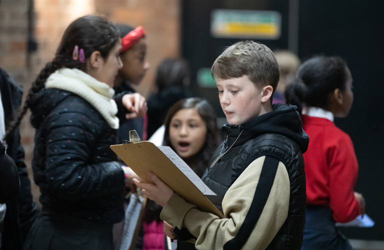 A group of primary school aged children, the one in focus is looking at a clipboard.