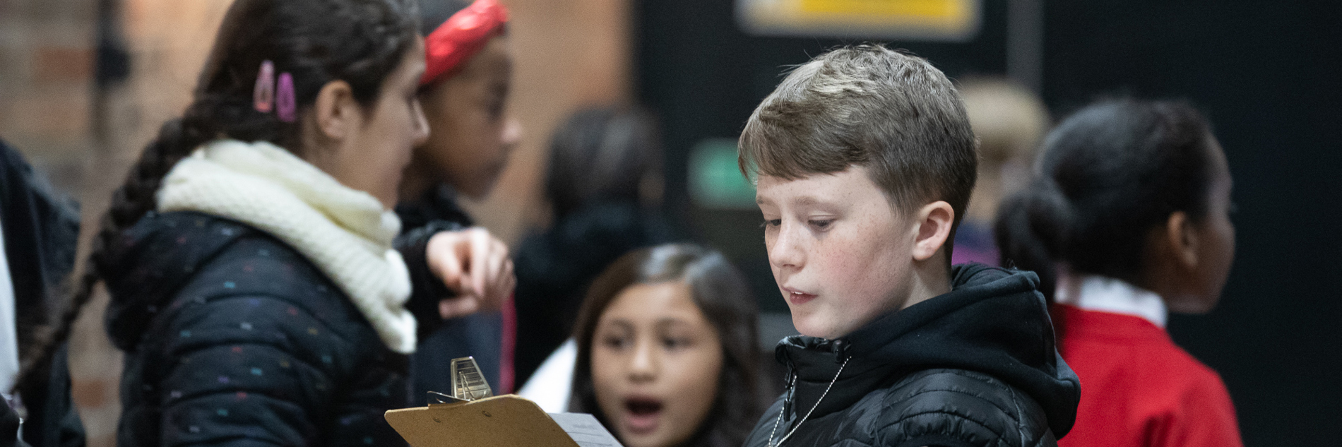 A group of primary school aged children, the one in focus is looking at a clipboard.