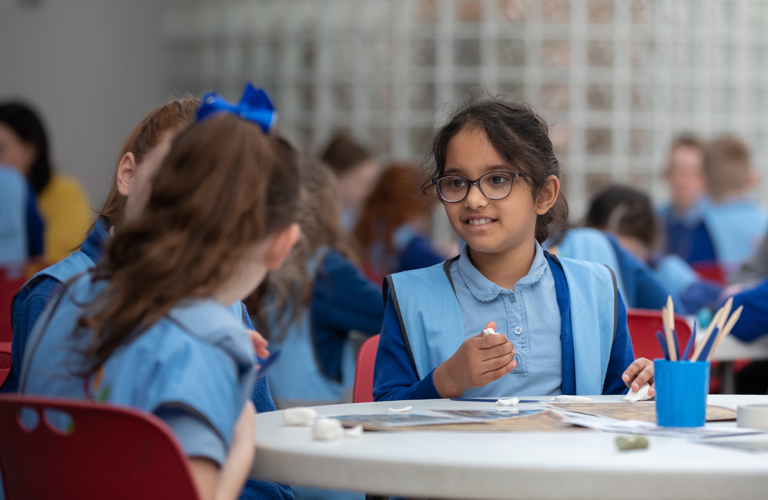 A group of children sitting at a table. On the table there is paper, clay and modelling tools. 