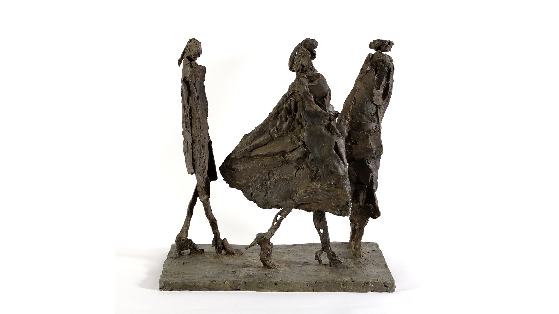 A photograph of a sculpture of three people caught in a walking motion. They are loosely sculpted in a brown medium