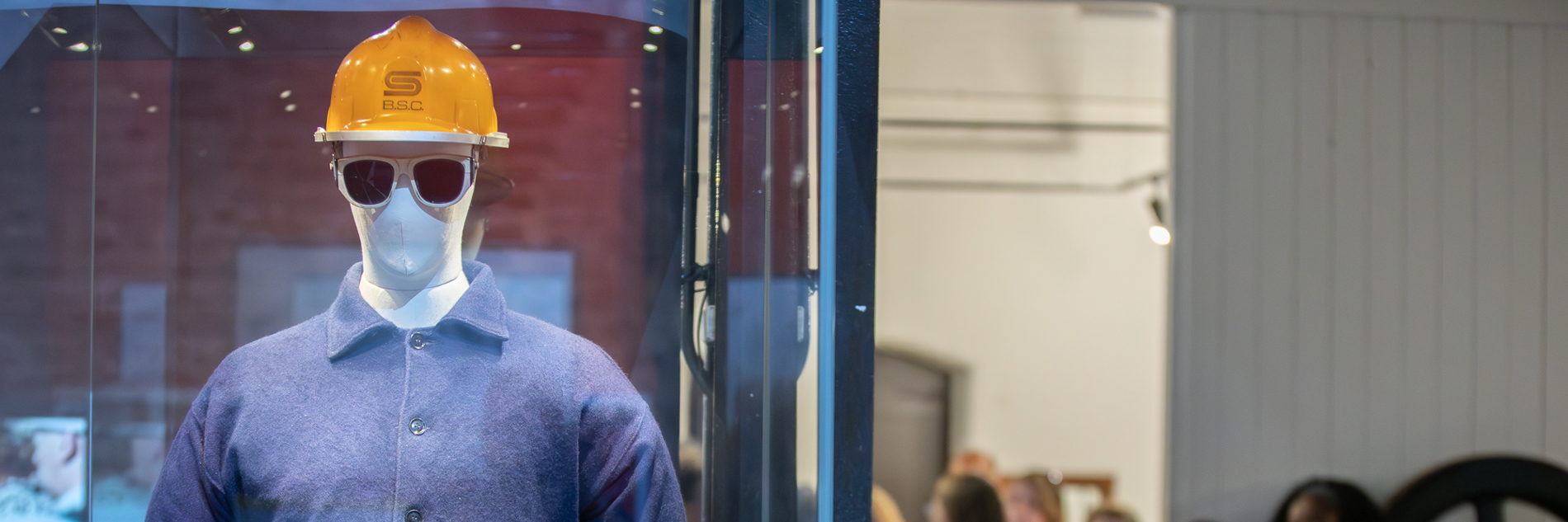A photograph of a mannequin wearing a blue boiler suit and a yellow hardhat