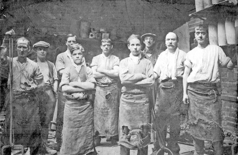 A black and white photograph of nine male steel workers, all looking defiantly into the camera.
