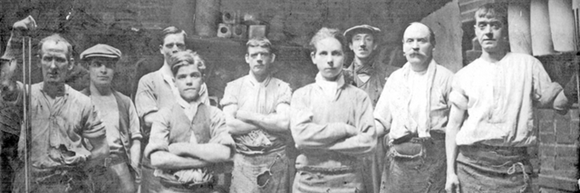 A black and white photograph of nine male steel workers, all looking defiantly into the camera.
