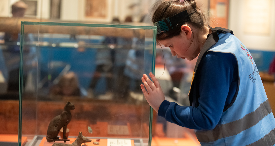 A child looking at Egyptian artefacts in a display case.  