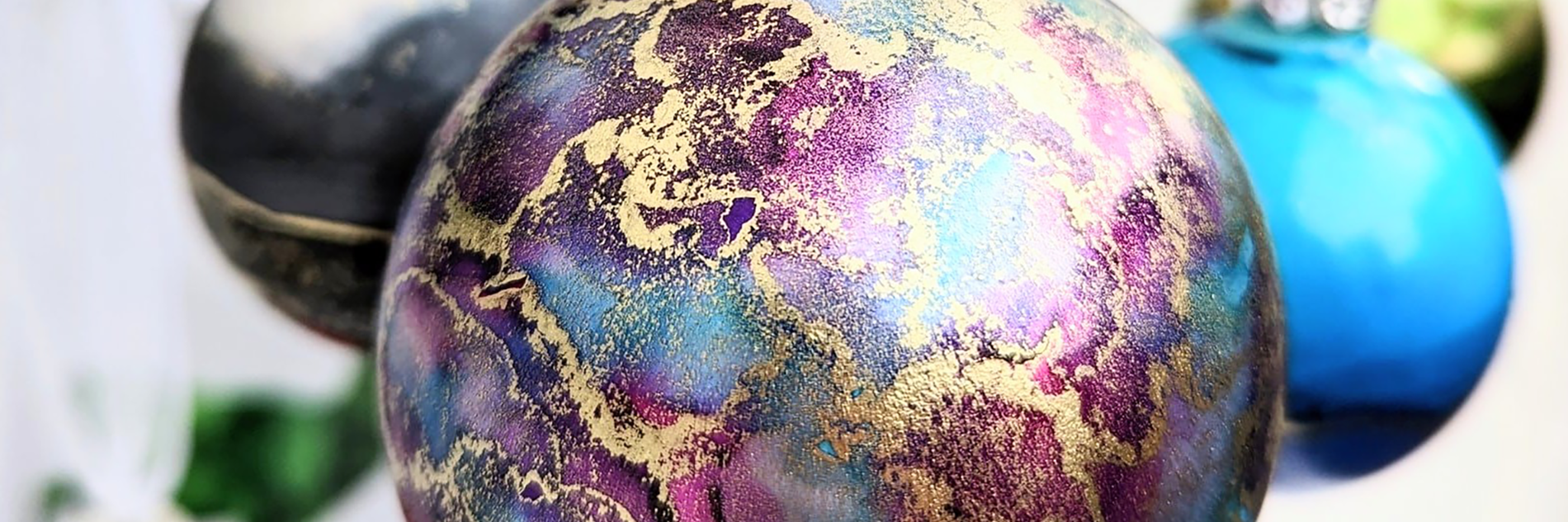 A close up of a purple bauble with swirls of gold and blue ink patterns. Other baubles can be seen in the background.