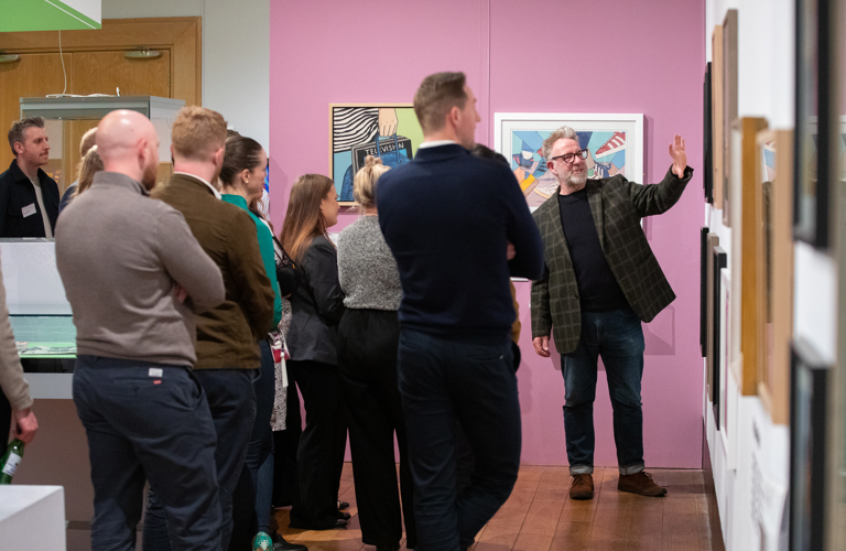 A group of people listen as an artist talks about his work in an art gallery 