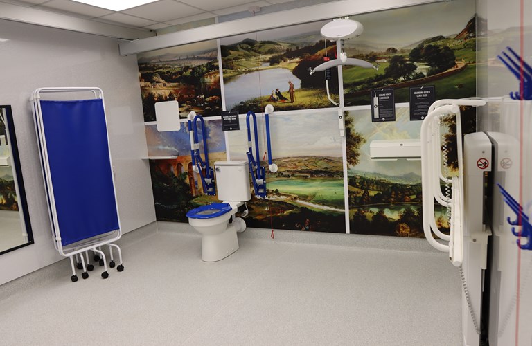The changing places toilet, showing half the room with some facilities pictured, including the toilet, grab rails, bed and hoist.